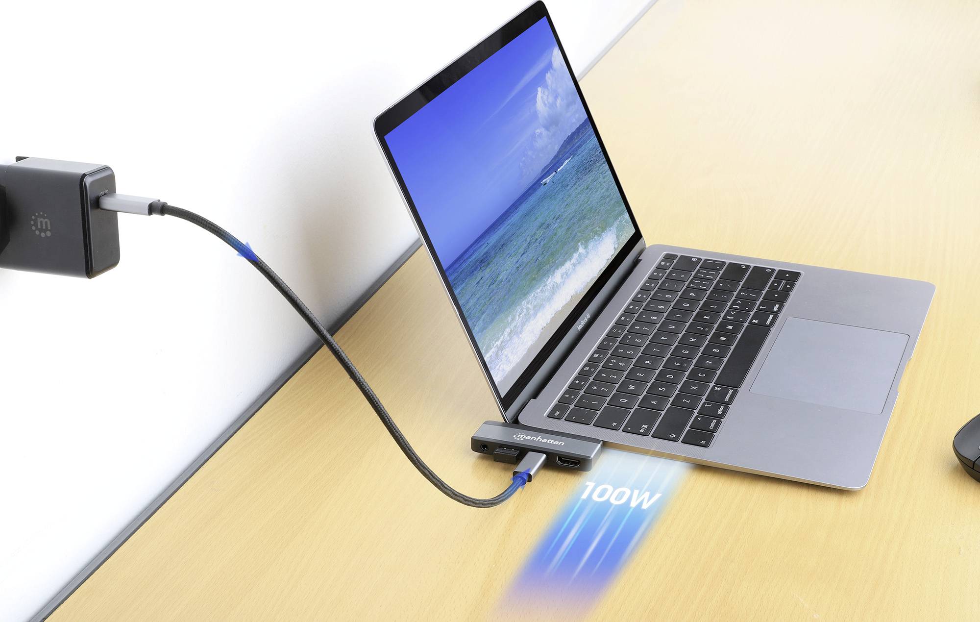 A laptop on a table is connected via a cable to an adapter displaying 100W, showing a seascape on the screen.