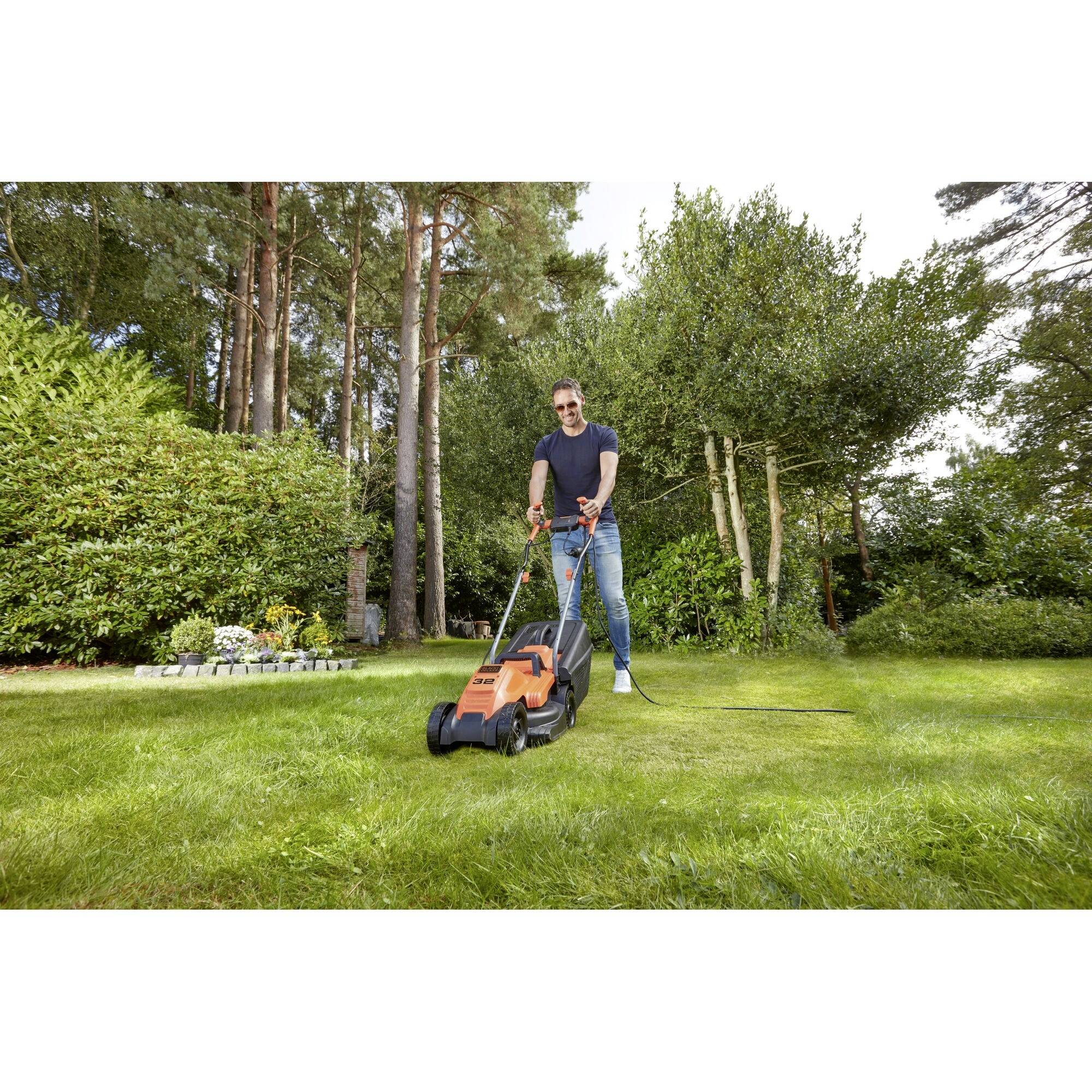 A person is mowing the lawn in a garden, surrounded by tall trees and bushes, with an orange lawnmower.
