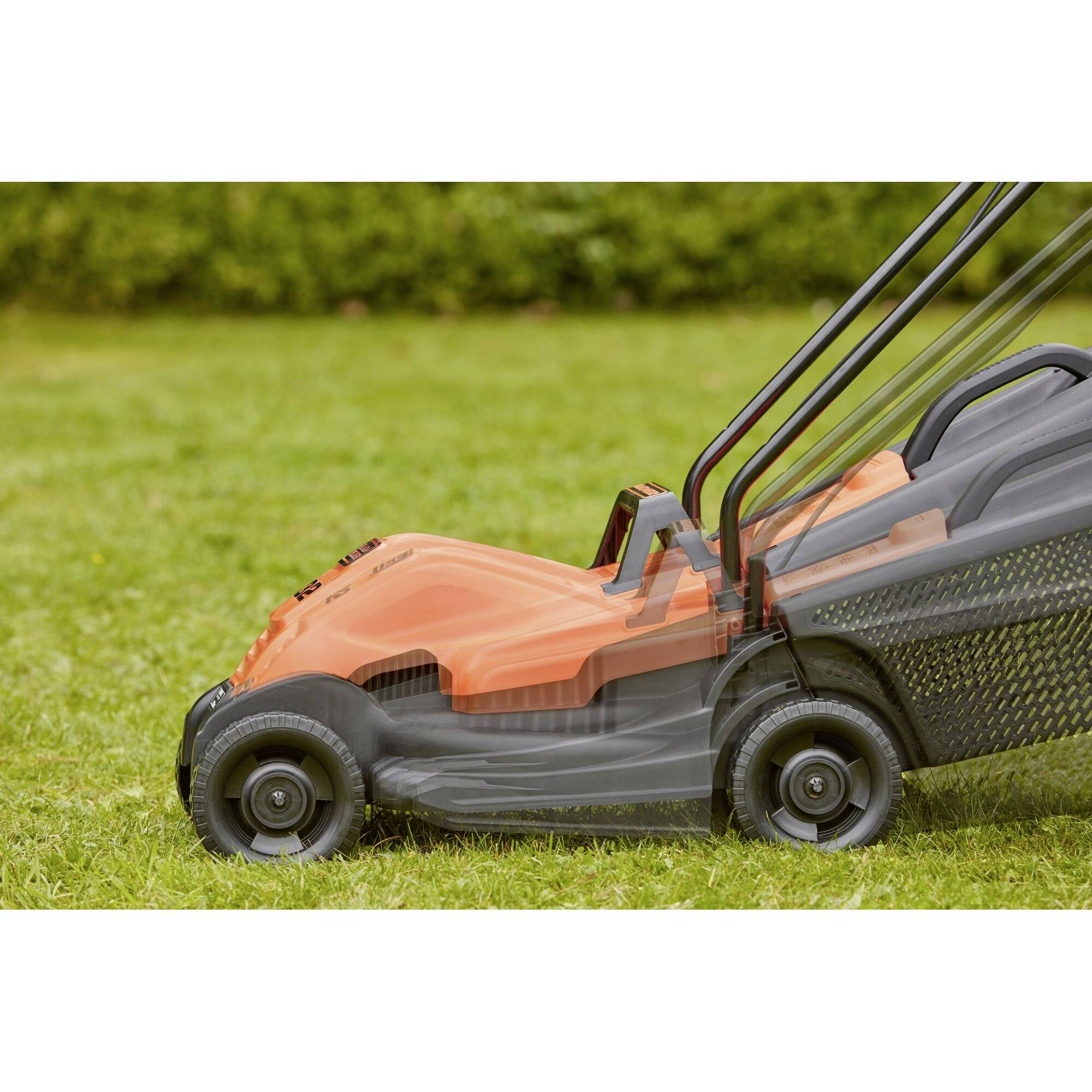 Lawnmower in profile on green grass. Clean lines and modern design with grass collection box. Blurred garden background.