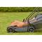 Lawnmower in profile on green grass. Clean lines and modern design with grass collection box. Blurred garden background.