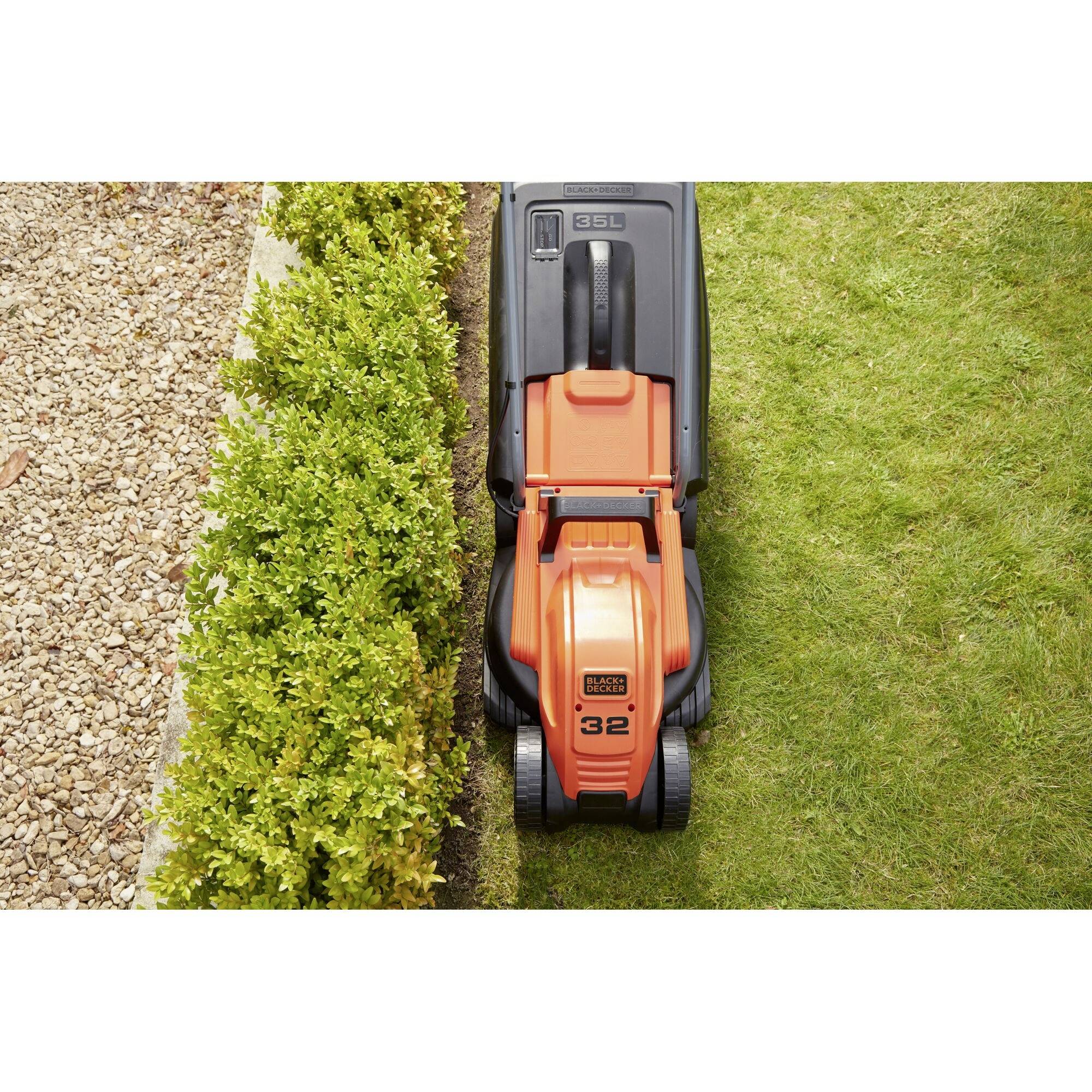 Lawnmower cutting grass next to a hedge, showing a clear distinction between the grass and gravel path.