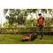 A person is mowing the lawn during the day in a garden with a lawnmower, wearing an orange hi-vis vest and a face mask.