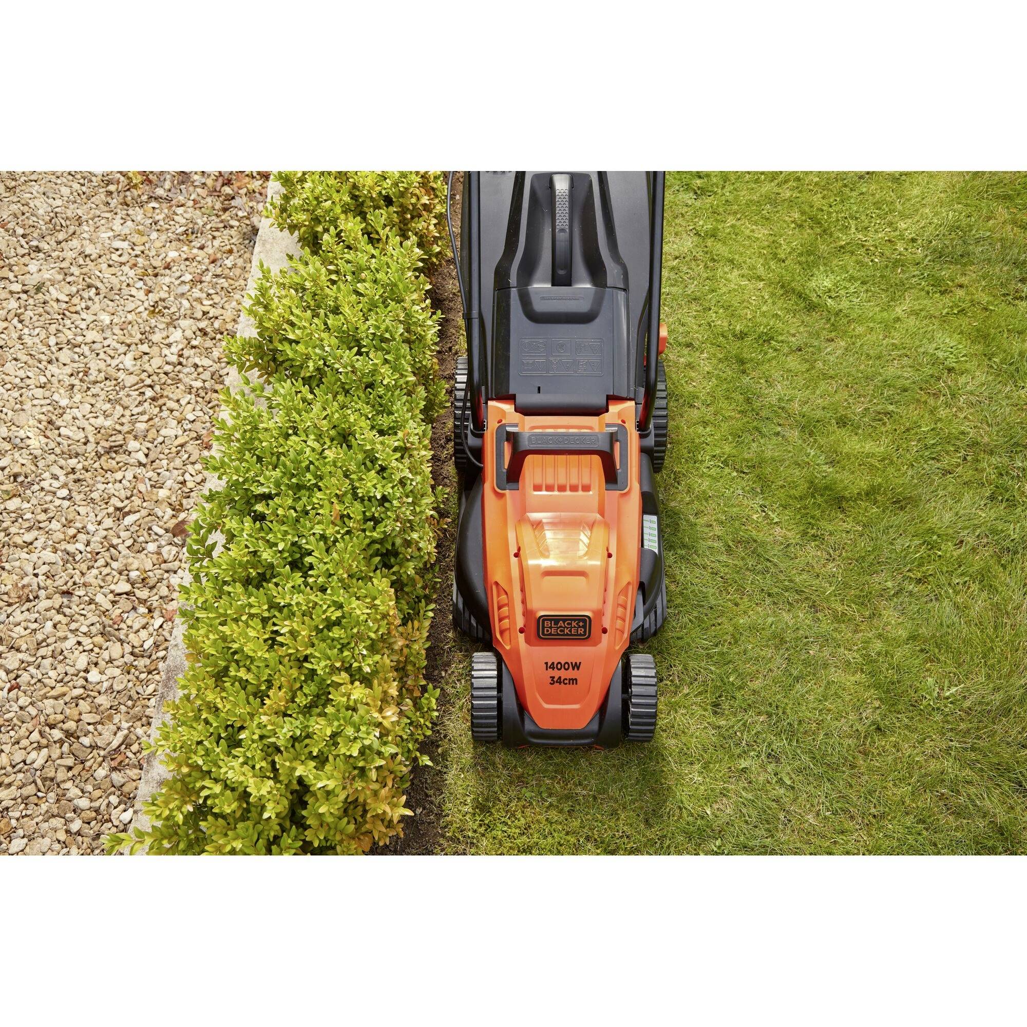 A lawnmower is cutting precisely at the edge between the lawn and a gravel path, next to a row of green bushes.