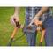 A person is gripping the handle of an orange-black lawnmower on a grassy area. The brand name is visible.