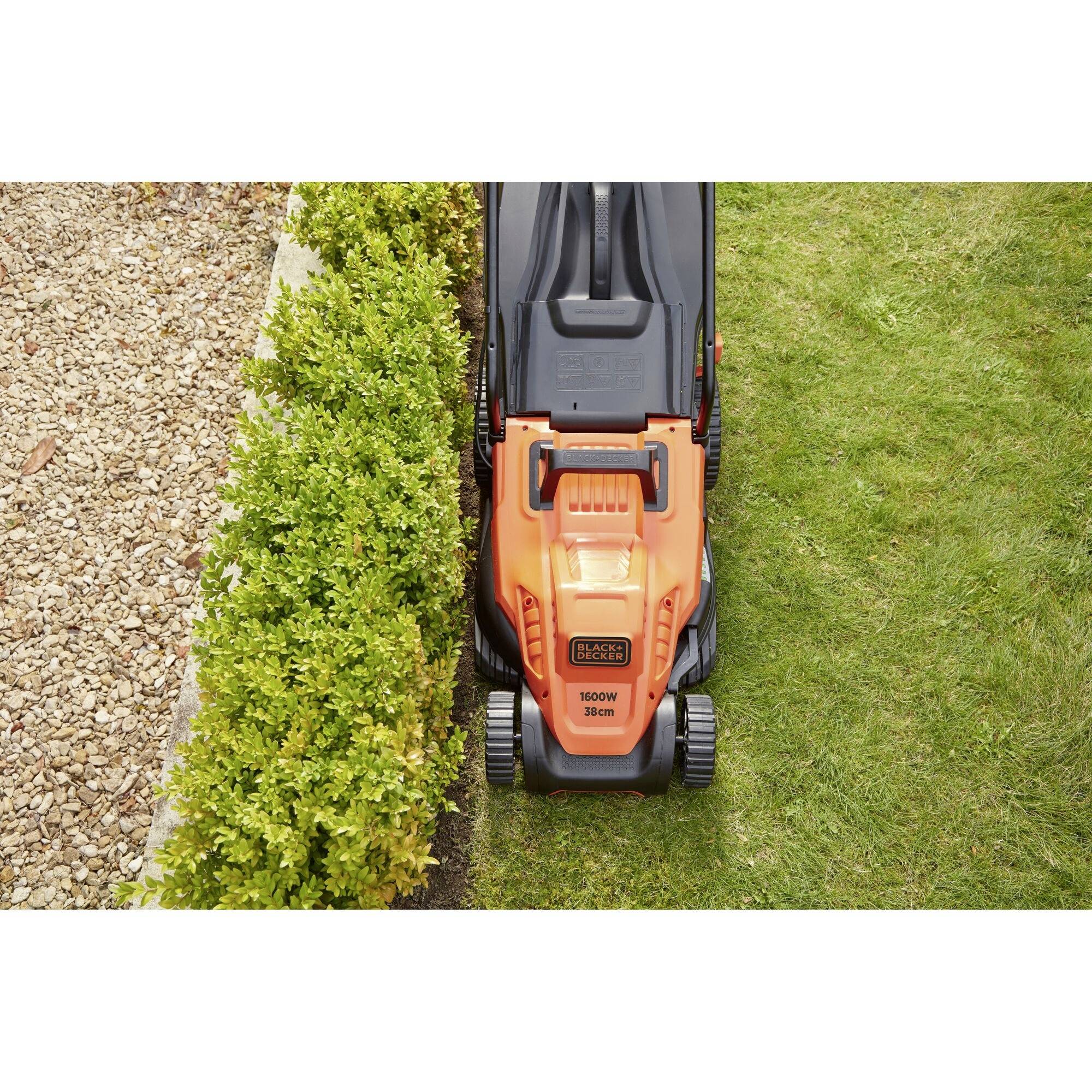 A lawnmower precisely trims the edge of a lawn beside a gravel path and a hedge, demonstrating its efficiency in garden maintenance.