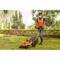 A person is mowing a lawn with an electric lawnmower in a garden. Wearing protective clothing, gloves, and a mask.