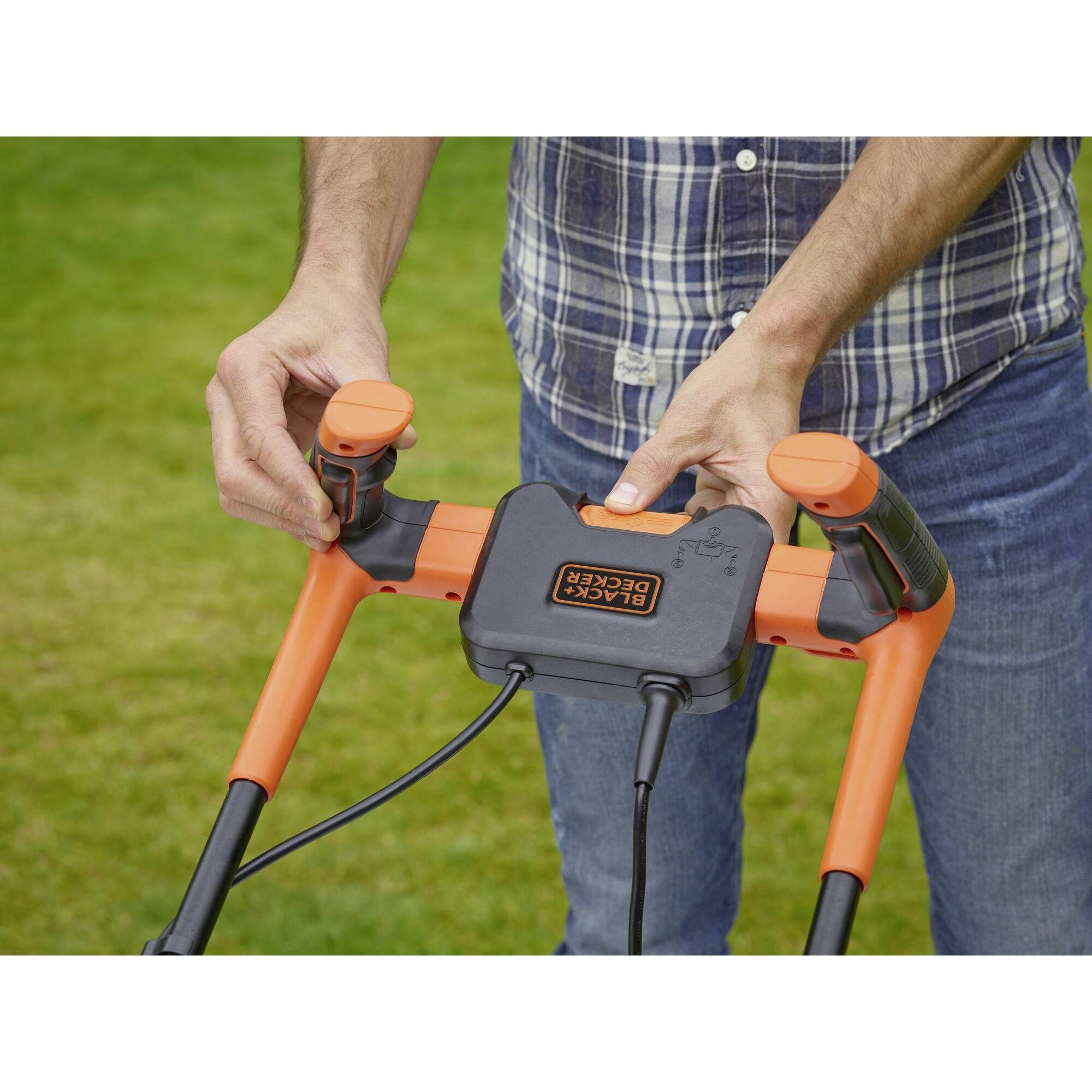 A person is holding the handle of an orange and black Black+Decker lawnmower, ready for use on a lawn.