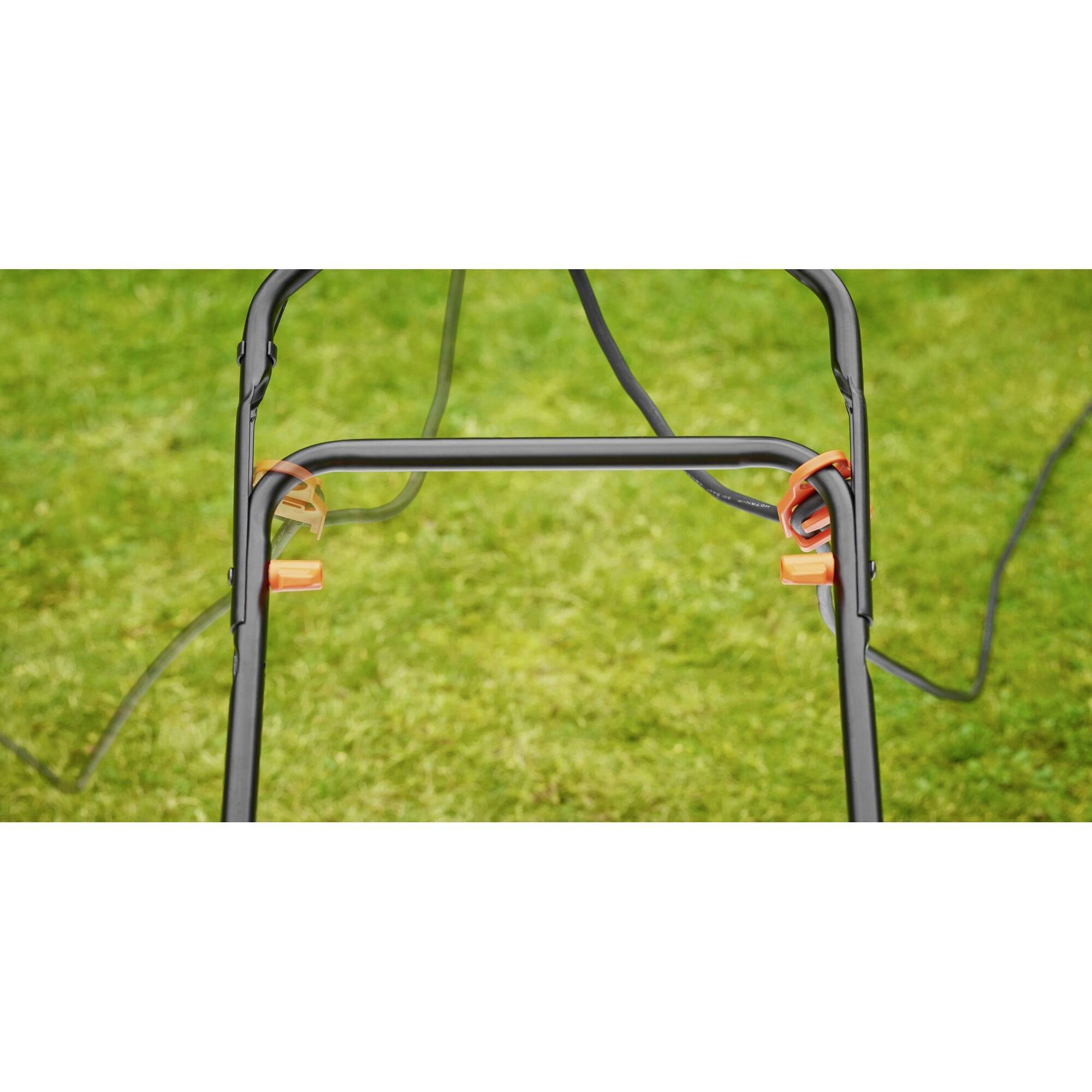 A verdant lawn with focus on part of a metal frame fitted with cable clips. The scene conveys a sense of gardening.