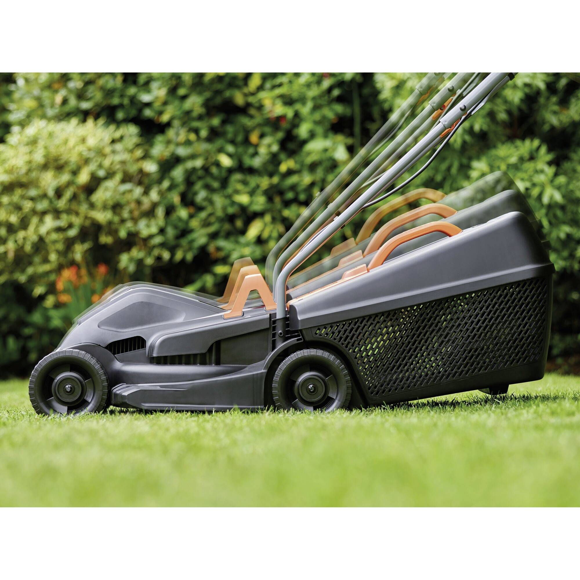 Lawnmower in the garden shows adjustable handle heights. Surrounded by green lawn and hedge in the background.