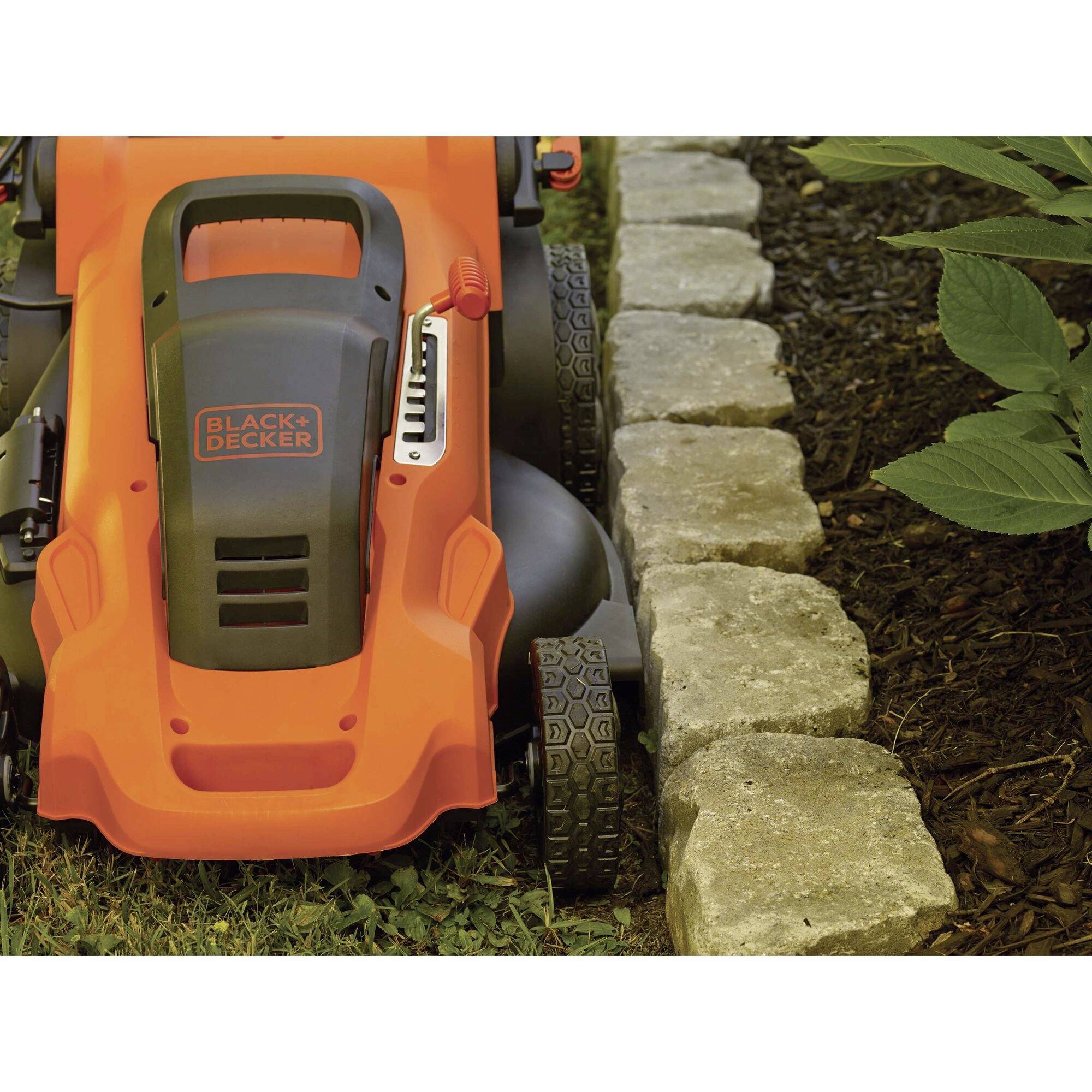 An orange lawnmower is cutting grass close to a stone-edged lawn area. The mower is positioned on the left, with the stone border on the right.