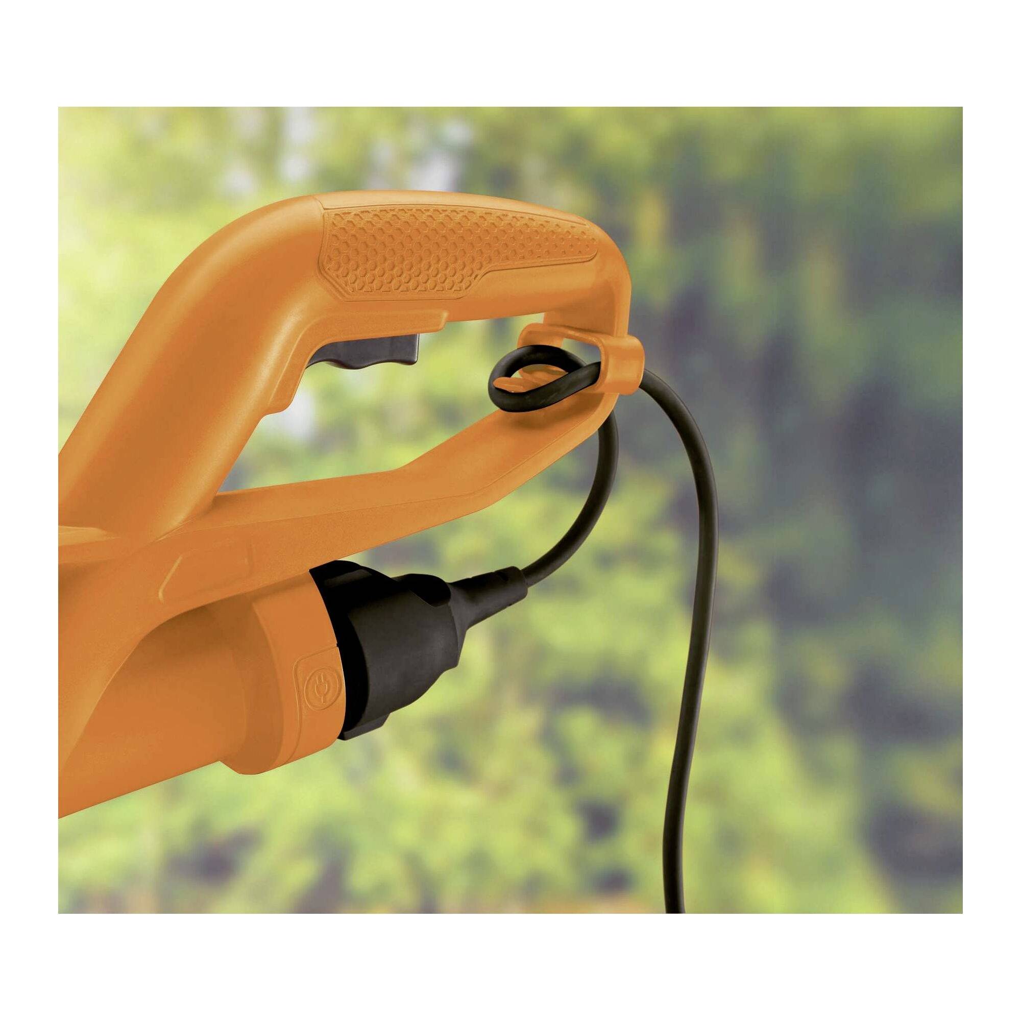 An orange electric lawn trimmer handle with a cable, with a blurred green background indicating a garden setting.