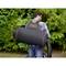 A man is wearing a black leaf blower backpack by Black & Decker and is vacuuming leaves in a garden with lush greenery in the background.