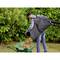 A person emptying garden waste from a leaf blower into a wheelbarrow, surrounded by lush greenery.