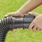 A man connects a black hose with another plastic component on green grass. The focus is on the hands and the hose.