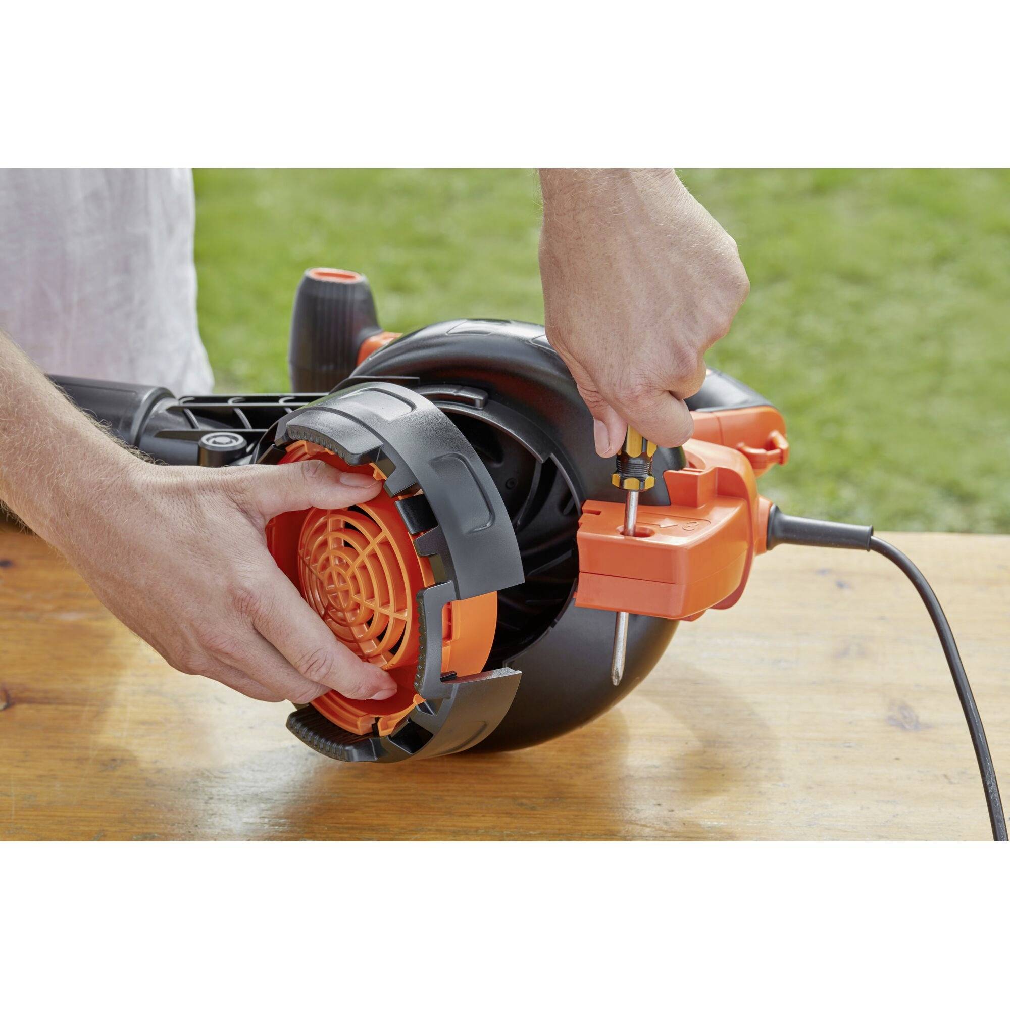A person is installing a garden tool attachment with a screwdriver on an outdoor table.