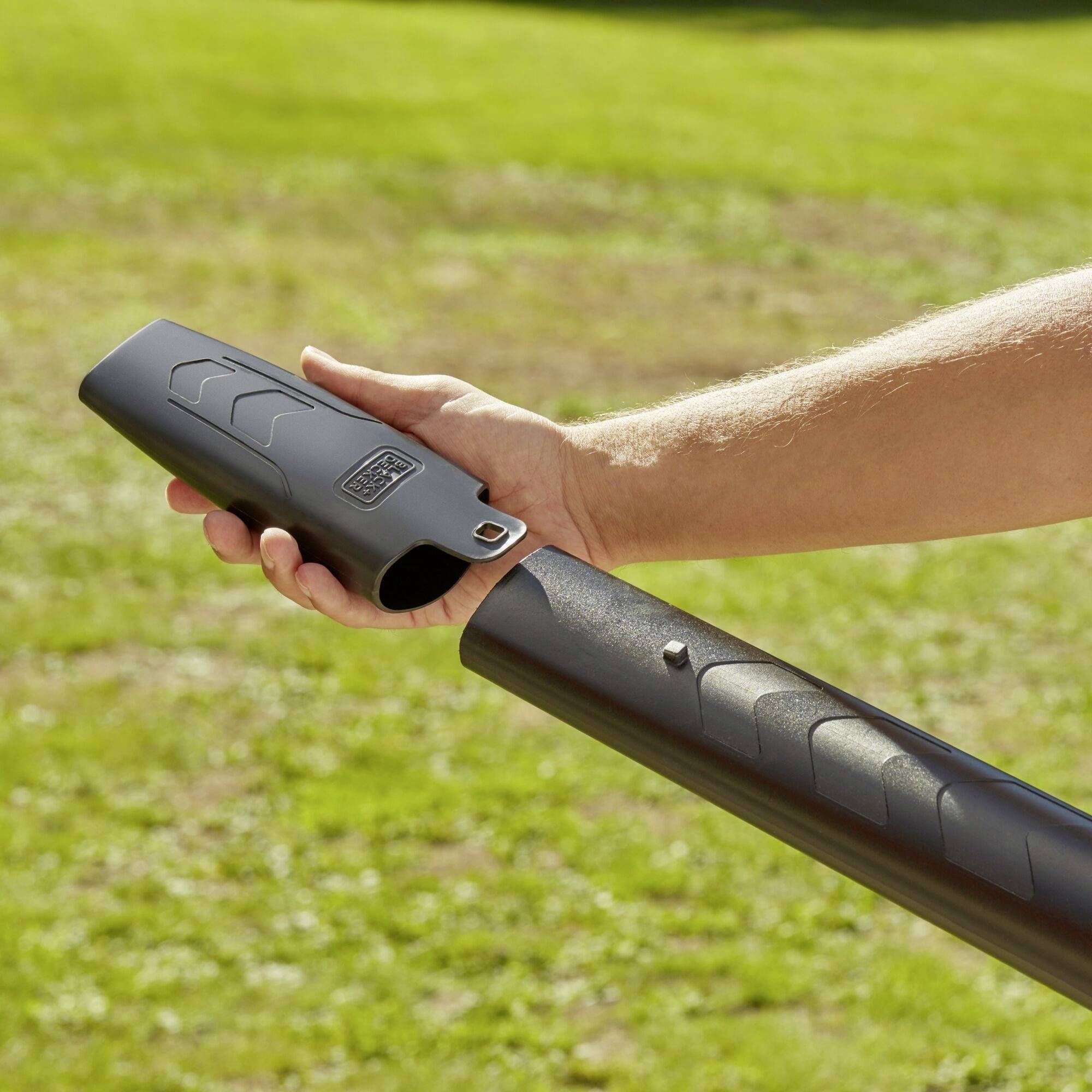 A person is mounting a cover onto a stovepipe in a garden. The main focus is on the hand and the pipe, surrounded by green grass.