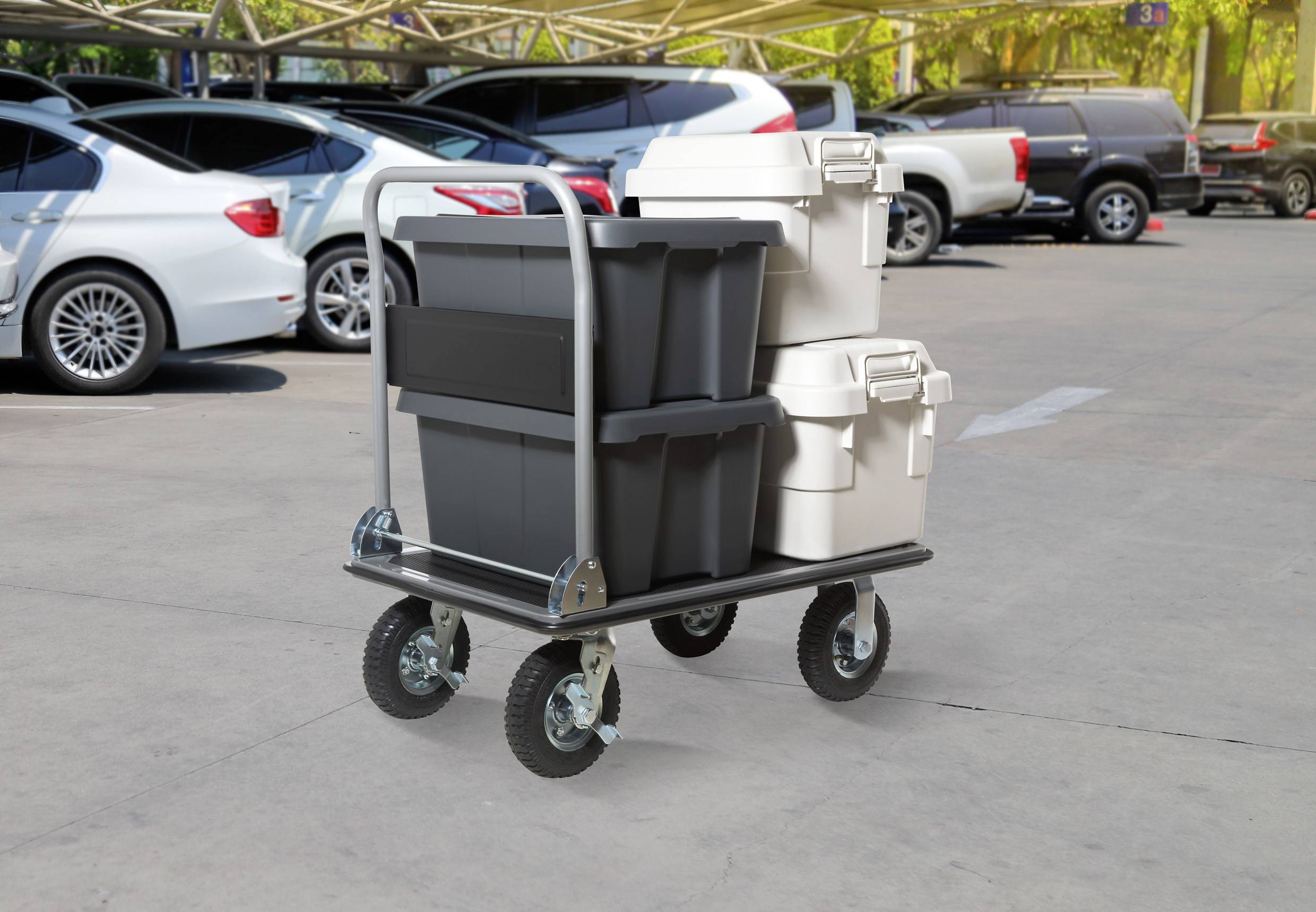 A utility cart with grey and white storage bins is parked in an outdoor lot with cars in the background.