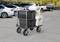 A utility cart with grey and white storage bins is parked in an outdoor lot with cars in the background.