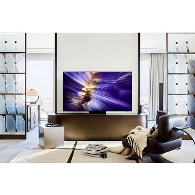 A modern living room with a large flat-screen television displaying an abstract image. In the foreground, a black armchair sits with a throw blanket.
