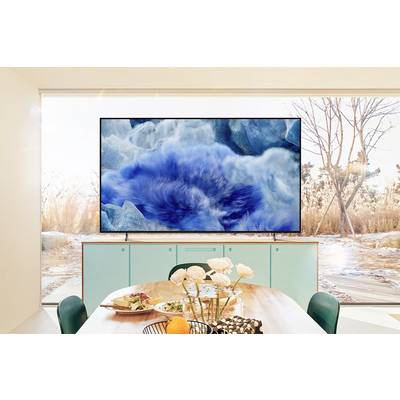 A television shows an image of blue waves. It stands on a cabinet in a room with large windows, through which nature can be seen.