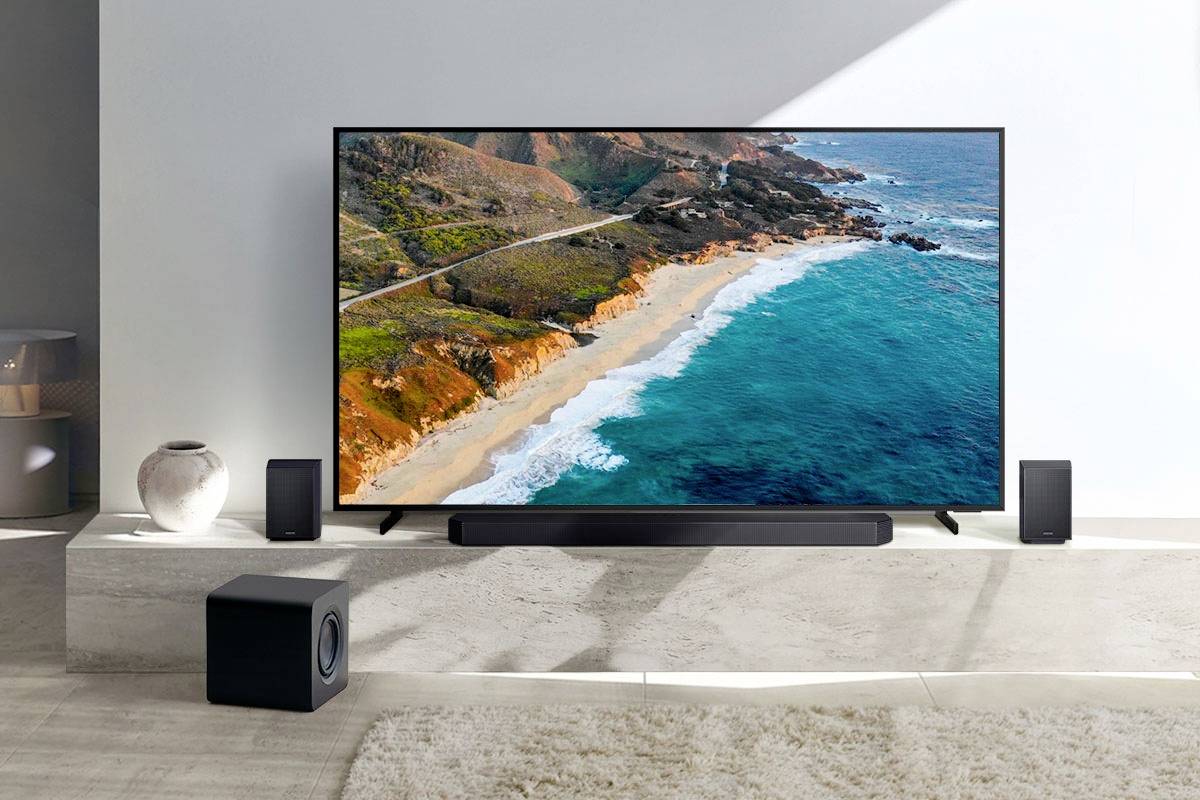A modern flatscreen television displays a coastal scene with clear blue water and cliffs. Surrounded by speakers in a living room.