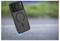 A black smartphone with a unique lens design and visible charging symbol on the case, levitating above a blurred outdoor surface.