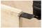 A power tool with a black blade is cutting through a piece of light-colored wood on a flat surface.