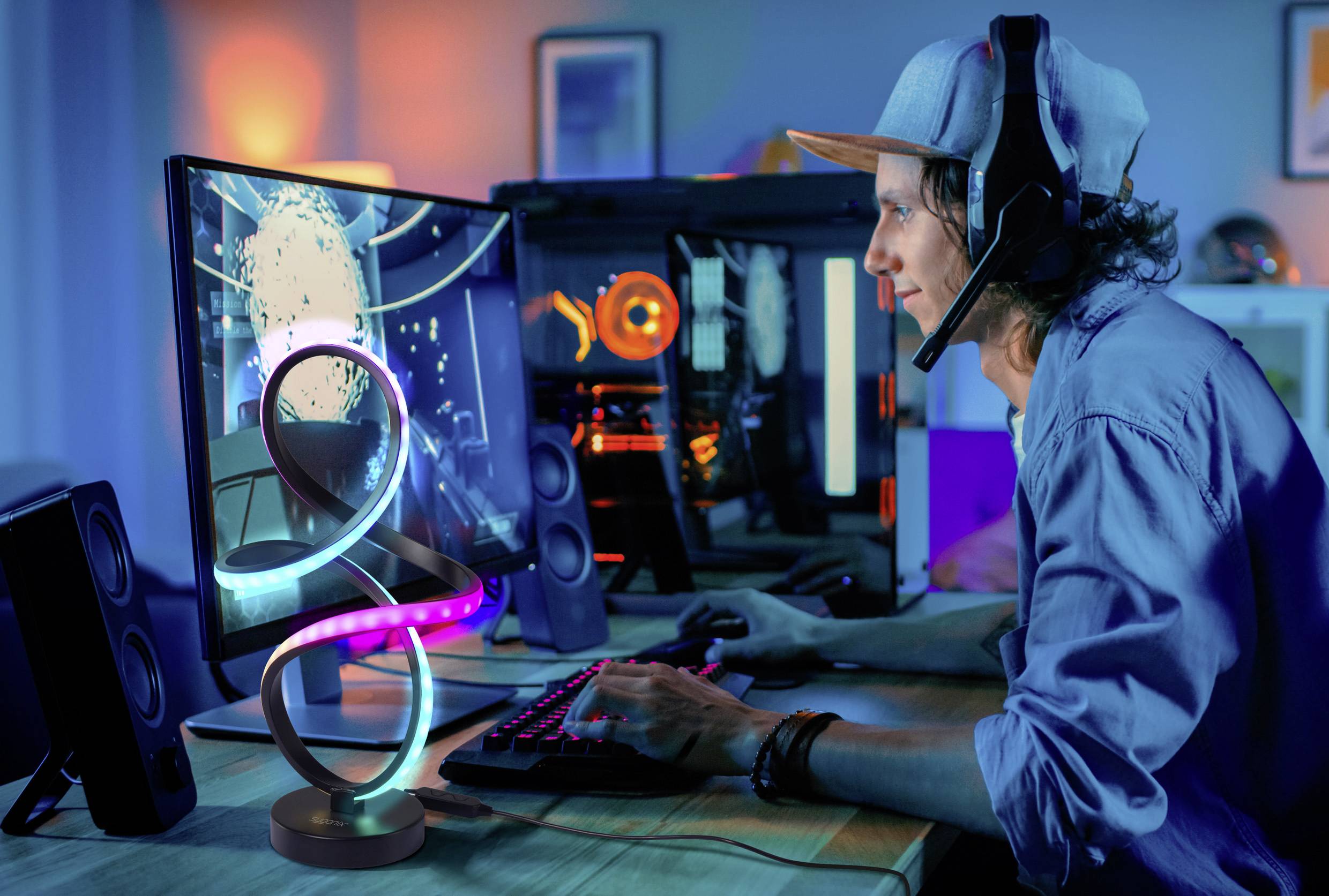 A person wearing a headset plays a video game on a computer, surrounded by a colorful, illuminated gaming setup in a dimly lit room.