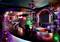 A vibrant nightclub with colorful neon lights, a glossy bar with high stools, a large mirror, and shelves stocked with bottles in a lively setting.