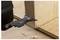 A close-up of a multitool with a saw blade attachment cutting through a wooden board, with wood shavings on the surface around it.