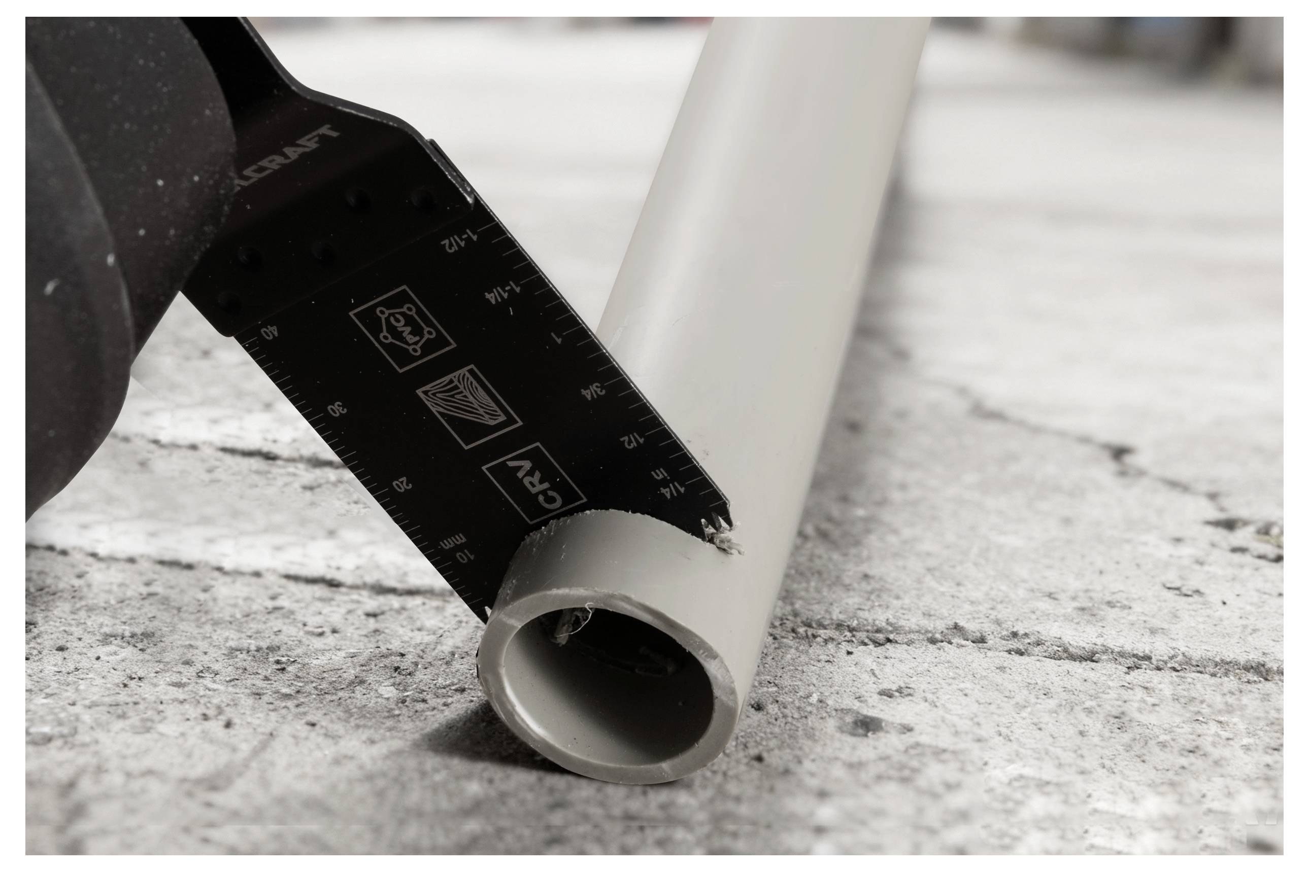 'A reciprocating saw blade cuts through a grey plastic pipe on a rough concrete surface, showing the tool in action for construction or repair.'