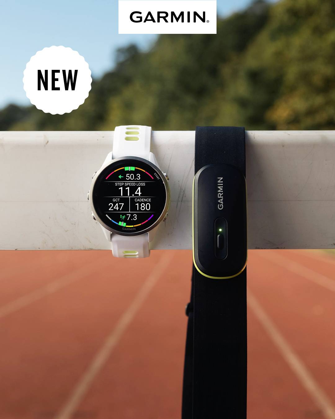 A Garmin smartwatch and a Garmin chest strap are placed on a railing in front of a running track. "NEW" appears in the top left.