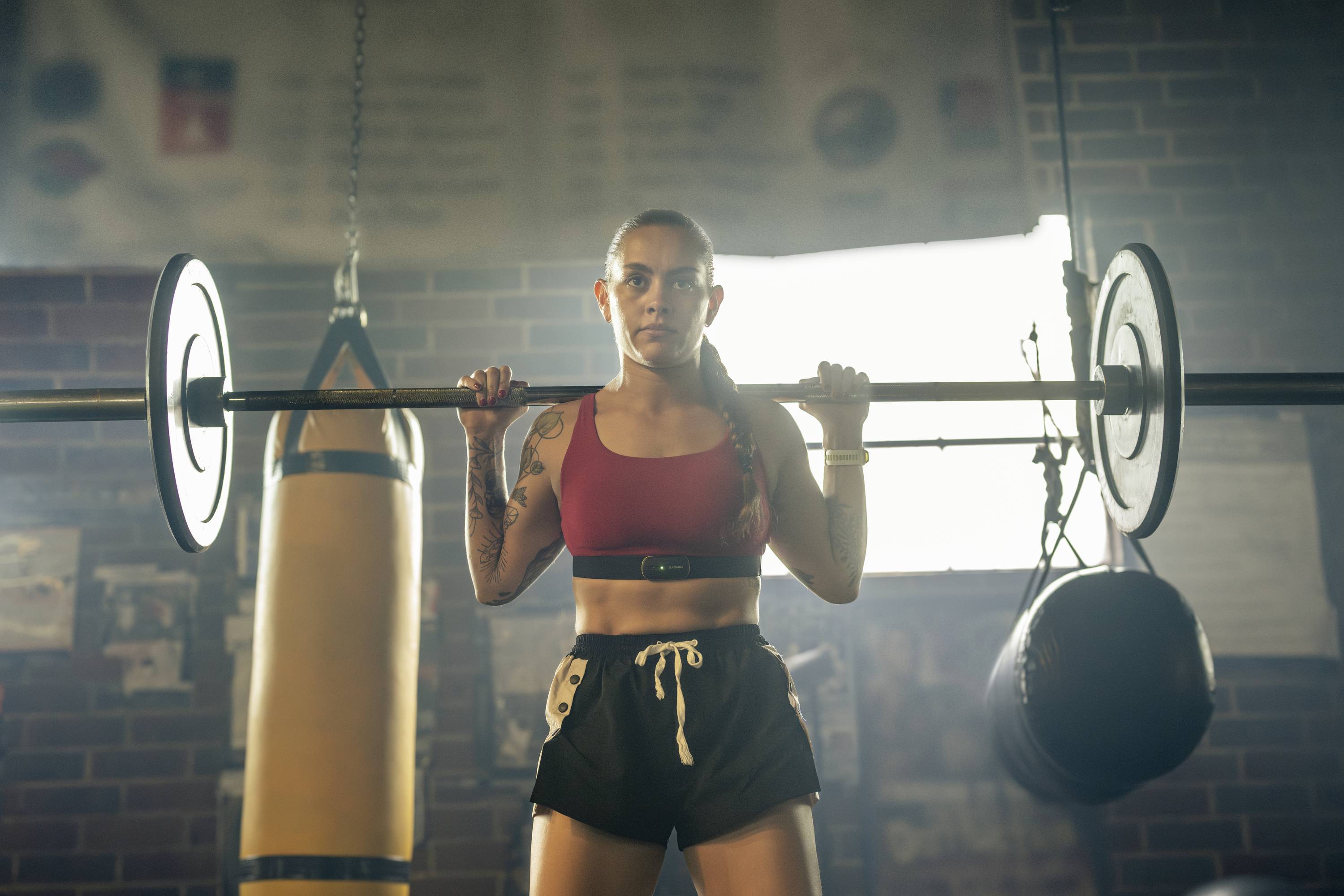 Woman in sportswear lifting a barbell in a gym. A punching bag can be seen in the background.