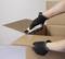 A person wearing gloves uses a safety box cutter to carefully open a cardboard box.