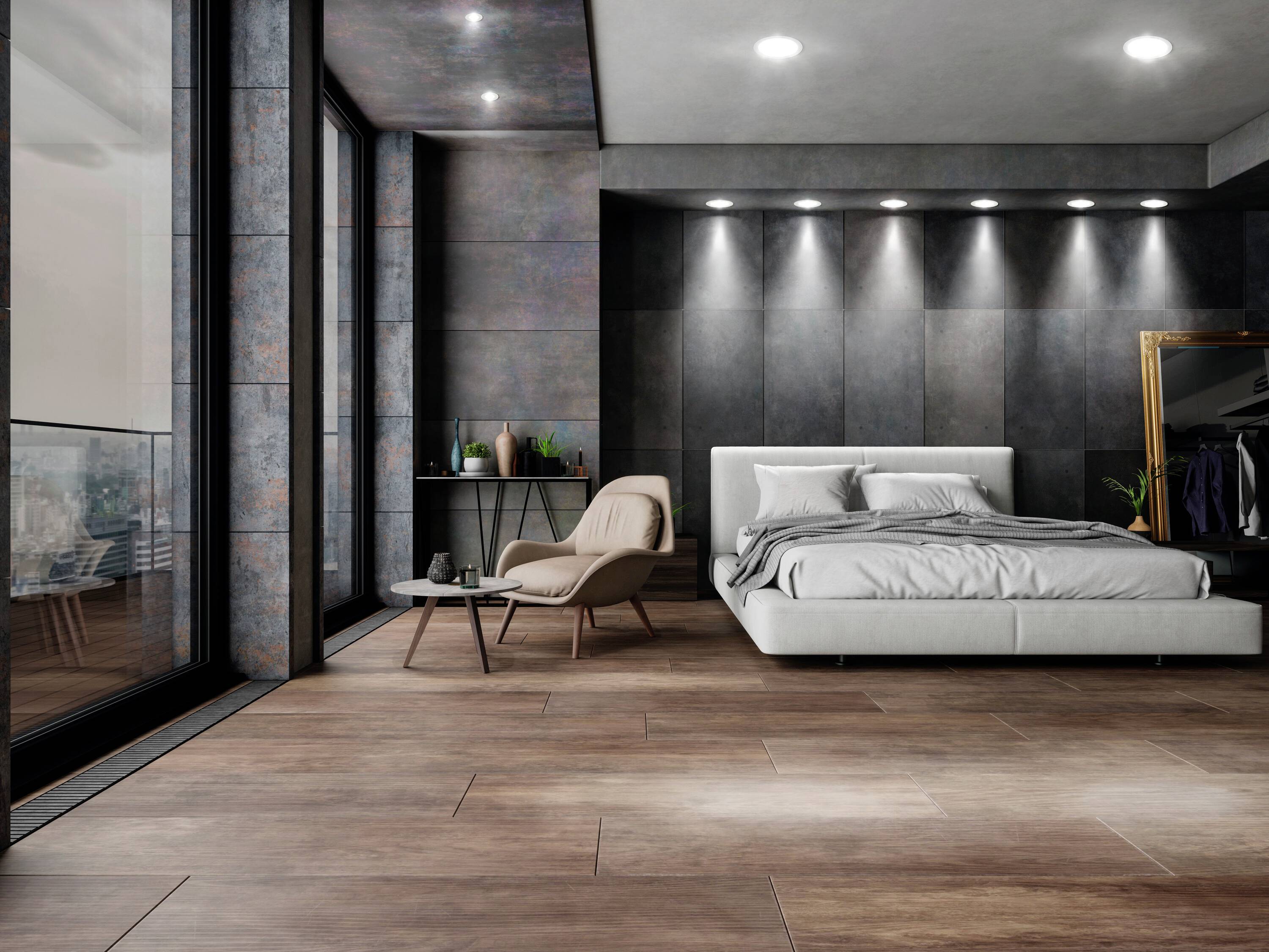 Elegant bedroom with large bed, armchairs, and vanity table. Dark, modern walls and wooden floors create a luxurious atmosphere.