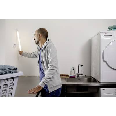 A man turns on the light in a utility room. He is standing next to a washing machine and a dryer.