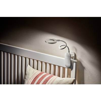A white bedside lamp with a flexible neck is clipped to the headboard of a white bed. A striped pillow lies on the bed.