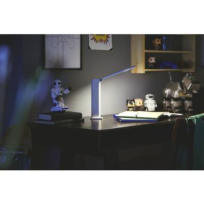 A desk with a lamp, open books, and toy robots. The scene is dimly lit, creating a cozy atmosphere.