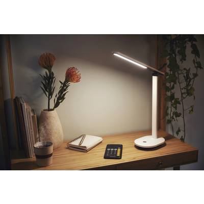 A well-lit desk with a desk lamp, notebook and calculator next to a vase with flowers.