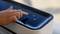 A hand operates the touch surface of a device with a large plus and minus symbol as well as an on/off switch in the center.