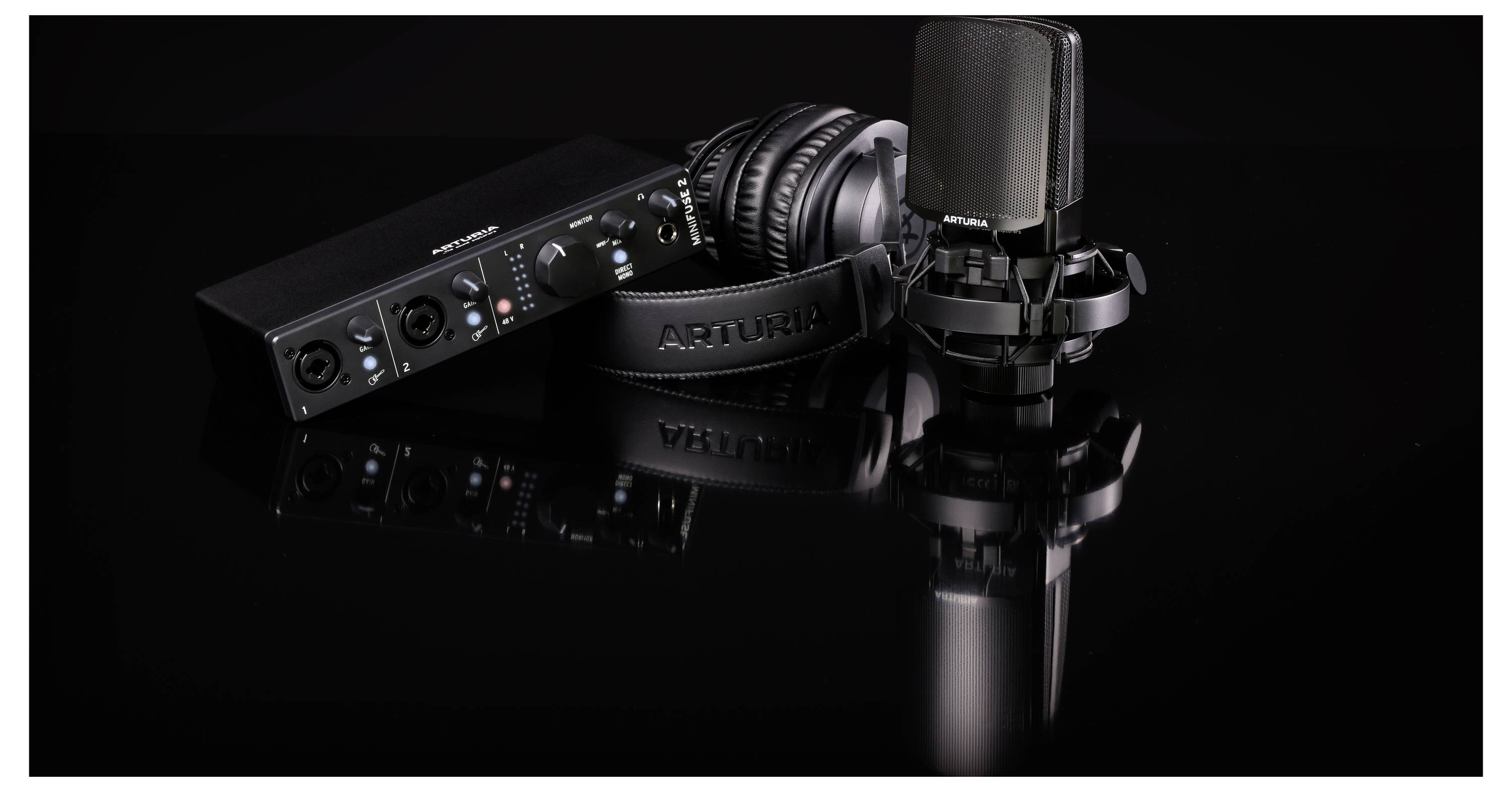 An audio interface, a microphone, and a pair of headphones are lying on a reflective surface.