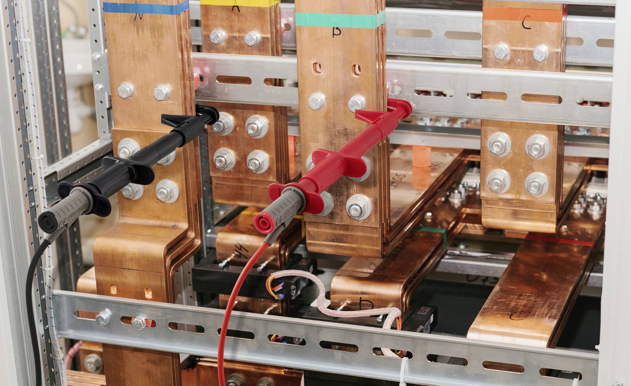 'Close-up of electrical busbars with red and black test probes attached, used for distributing electricity within a power cabinet.'