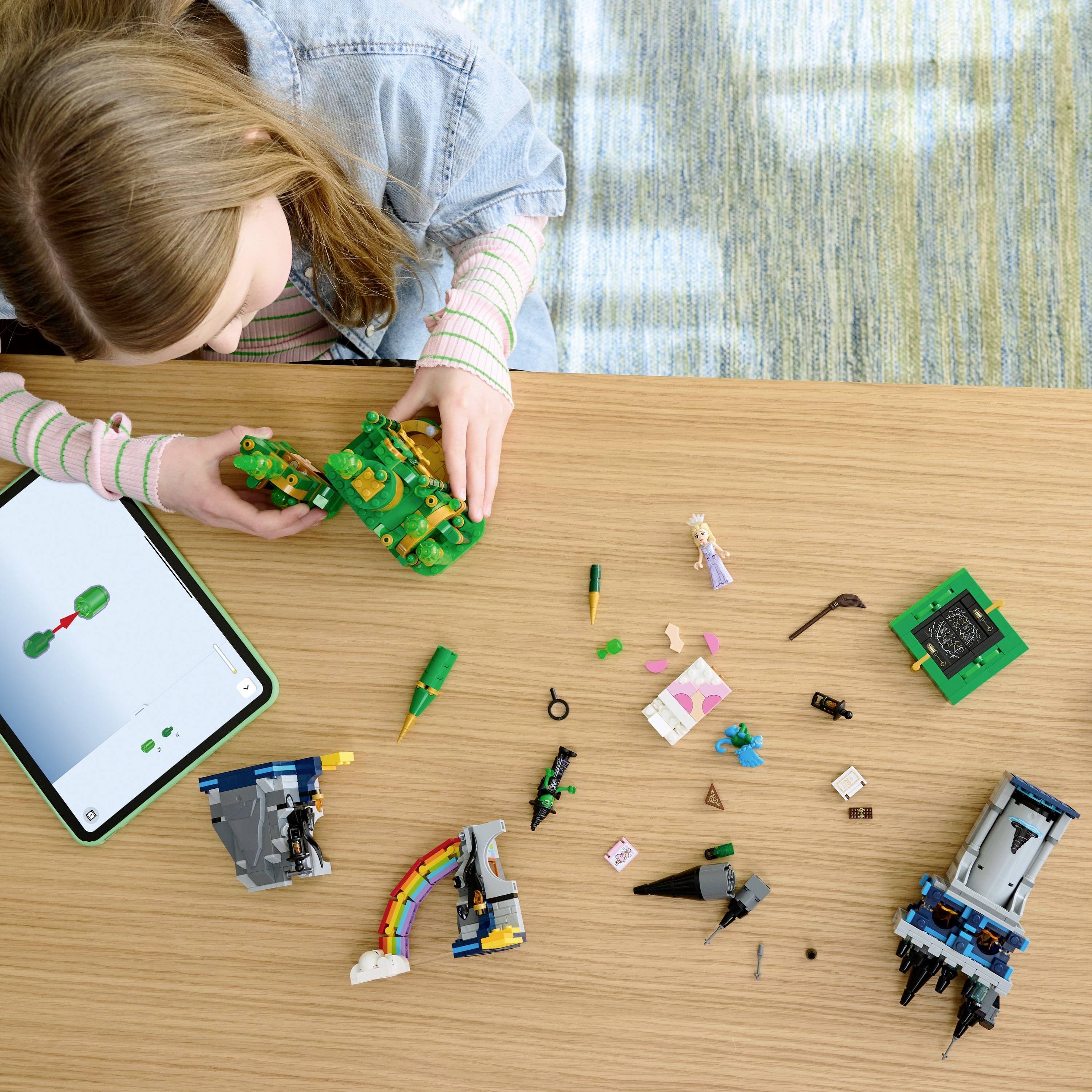 A child engages in building models with a construction set on a wooden table. A tablet displaying instructions lies nearby.