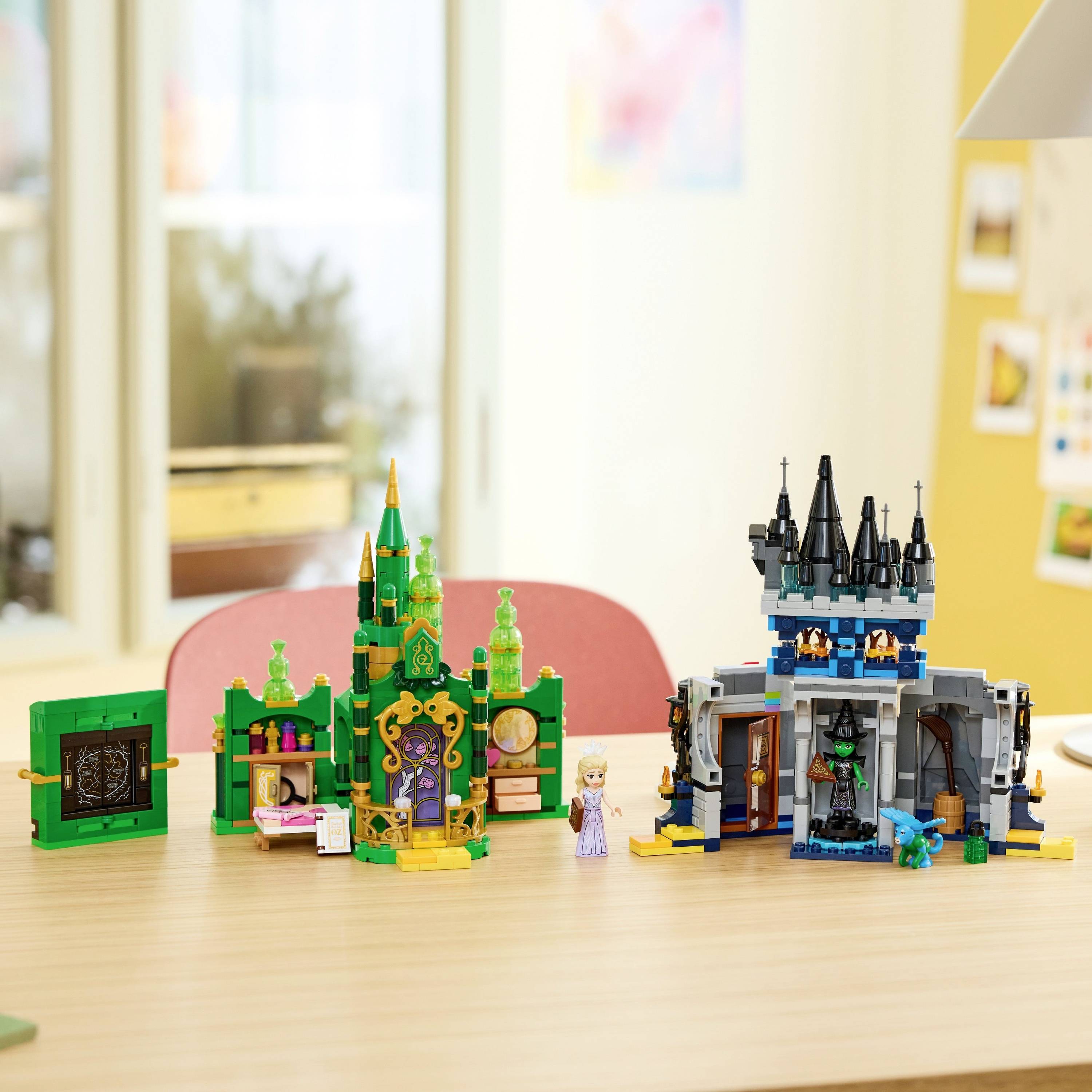 Toy castles on a desk with colorful, detailed designs. Figures from a well-known fairy tale stand between the castles. Indoor setting.