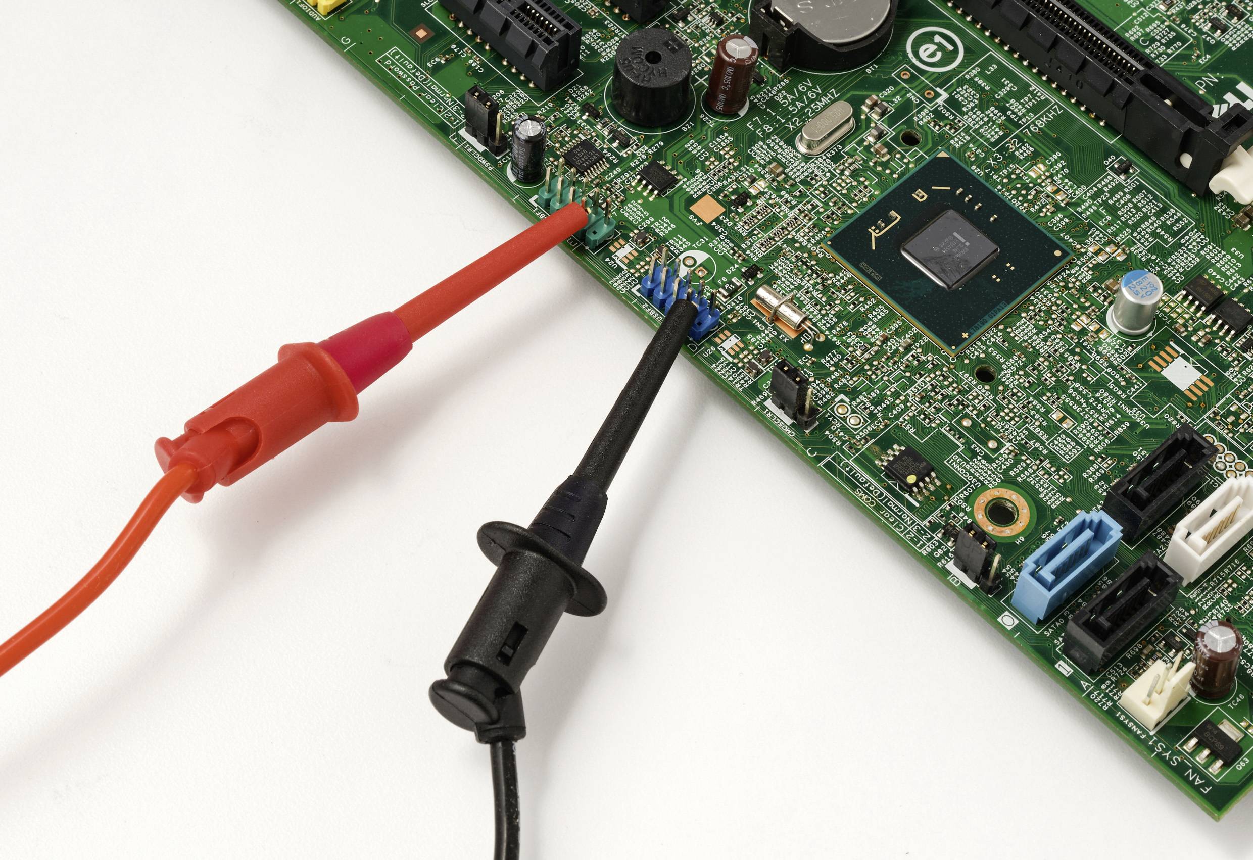 Two multimeter probes in red and black test a circuit board densely populated with electronic components, highlighting diagnostic analysis.