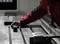 A person in a red jacket operates a metalworking machine, adjusting a component on a metal table inside an industrial setting.