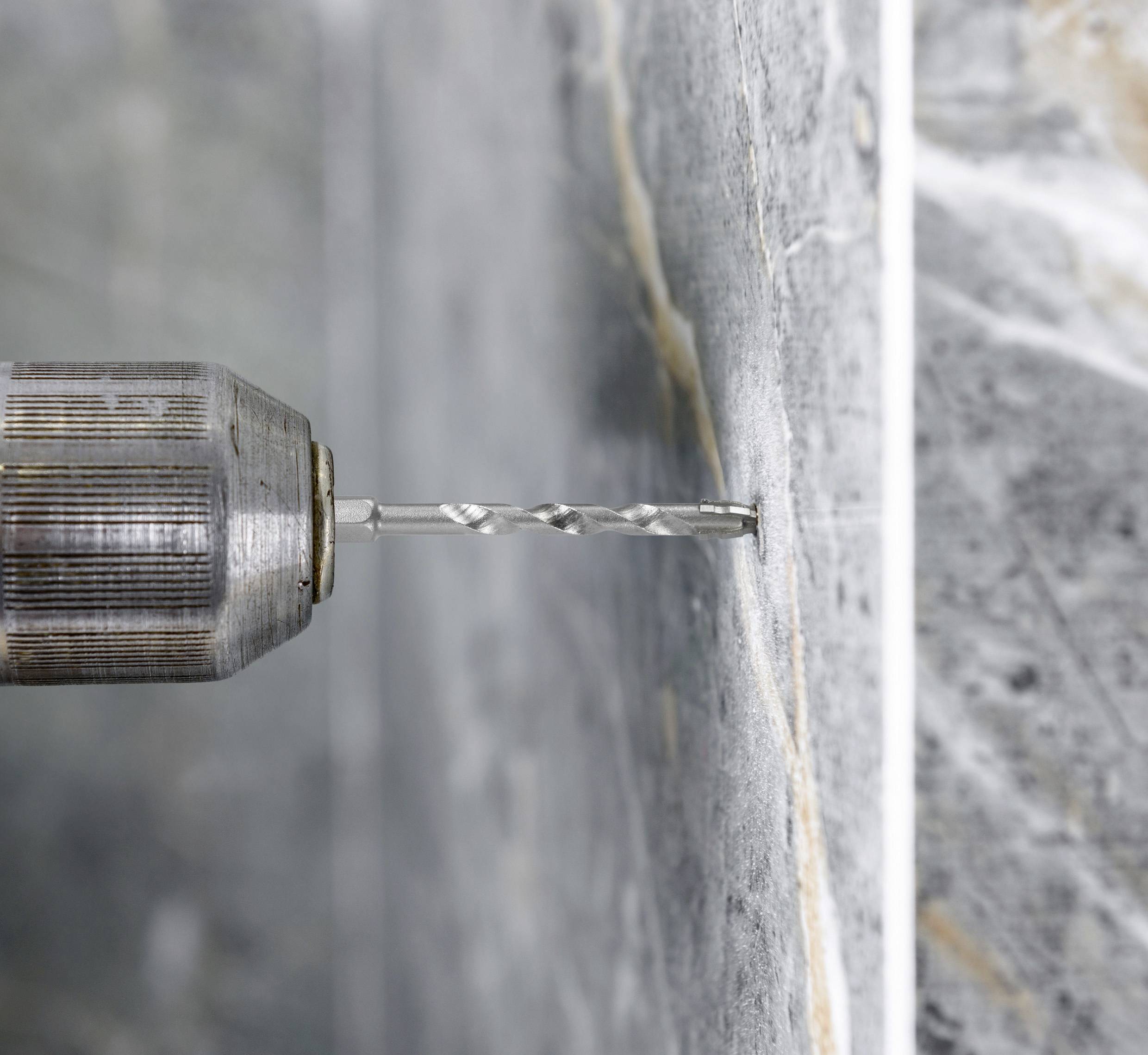 'A drill is making a hole in a concrete wall.'