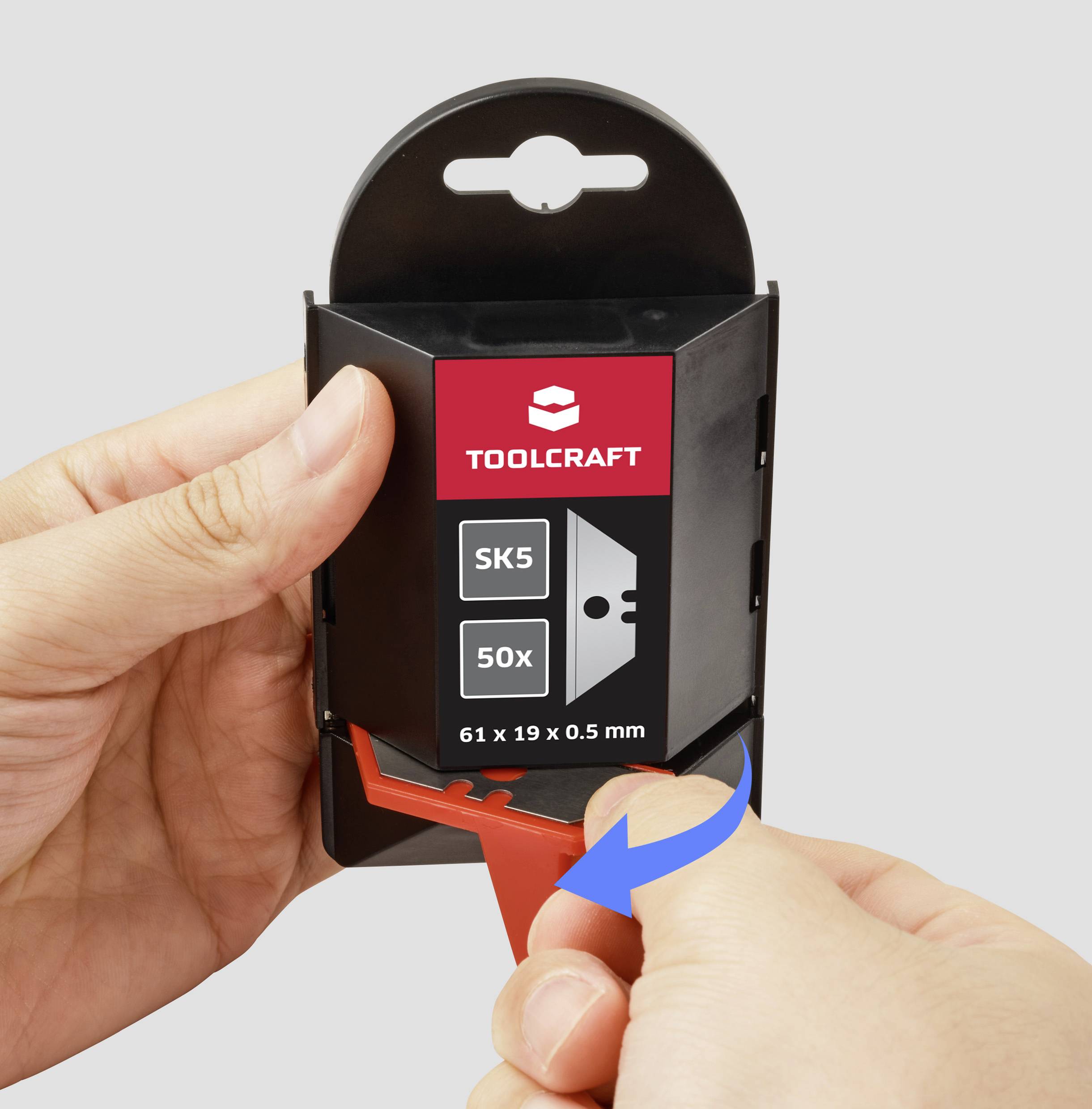 Hands opening a package of TOOLCRAFT utility knife blades labeled 'SK5 50x, 61 x 19 x 0.5 mm', with a blue arrow indicating direction.