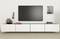 Modern living room setup with a flat-screen TV mounted on a white wall. Below, a minimalist white media console holds decor items.