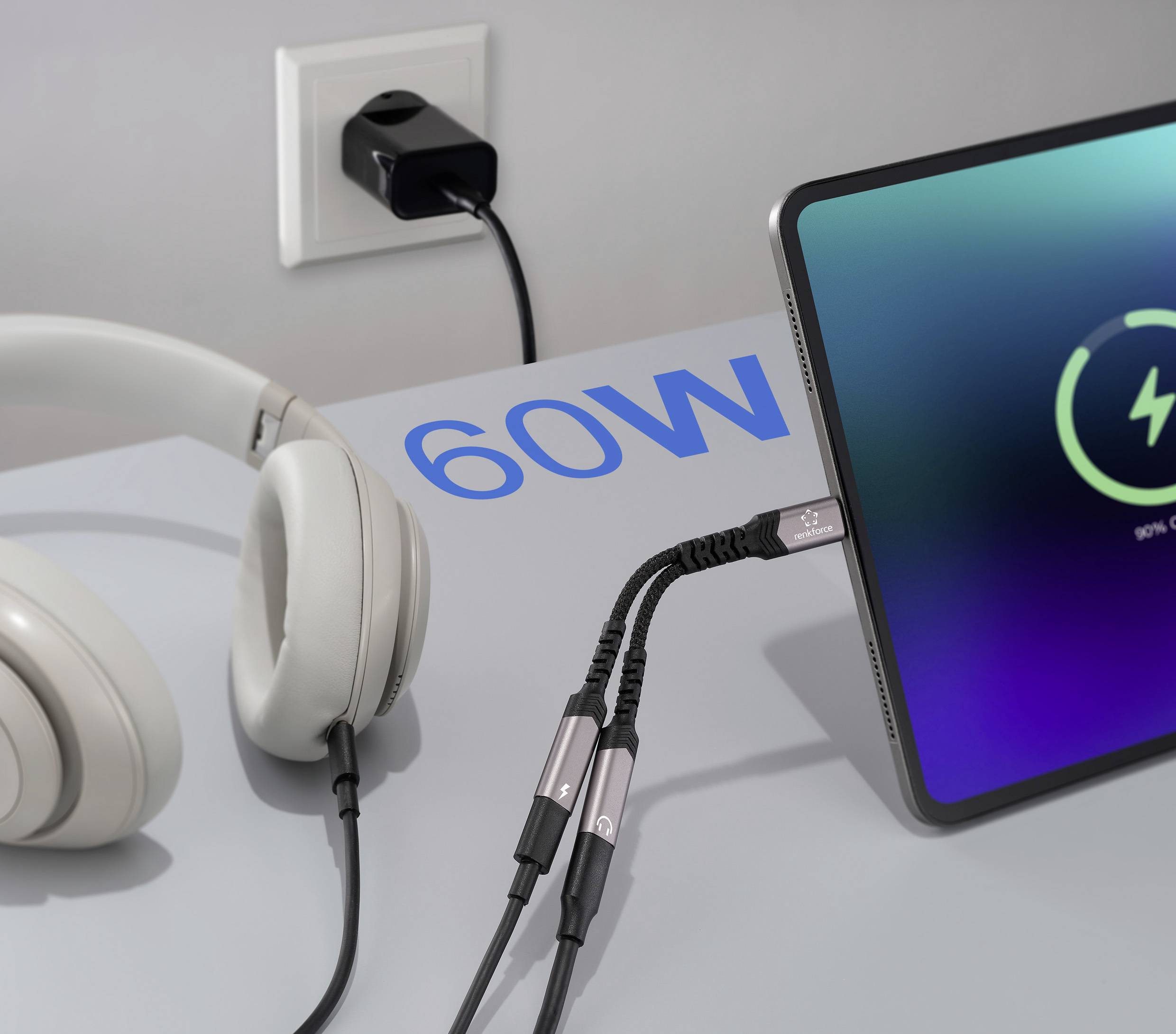 A tablet is charging on a desk beside headphones. The screen displays a charging symbol, and '60W' is written on the desk, indicating power output.